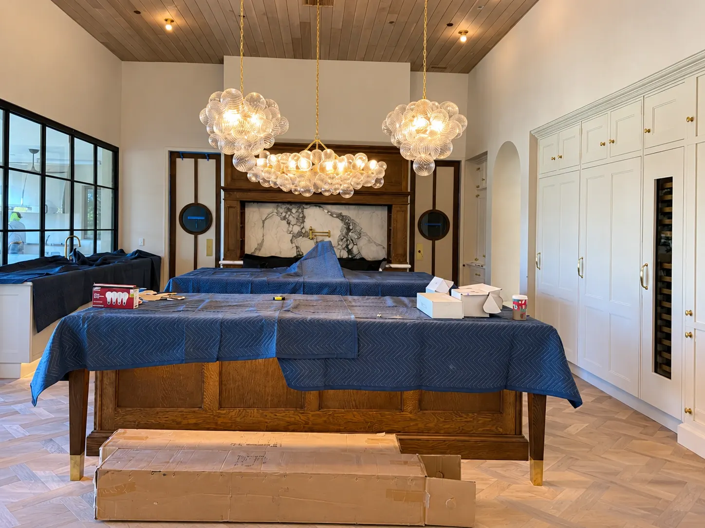 Luxury bedroom with two wooden beds covered in blue quilts, glass bubble pendant lights, marble fireplace, and white built-in cabinetry