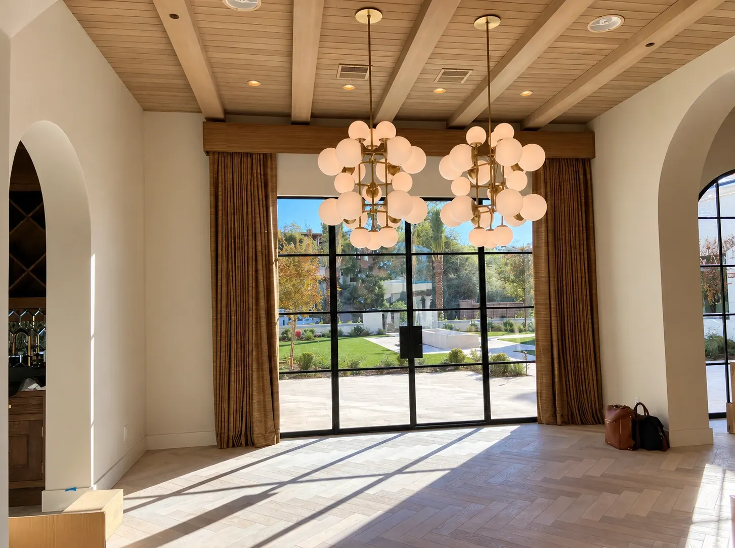 Modern luxury interior with two cluster pendant lights, wooden ceiling beams, and floor-to-ceiling windows overlooking manicured grounds